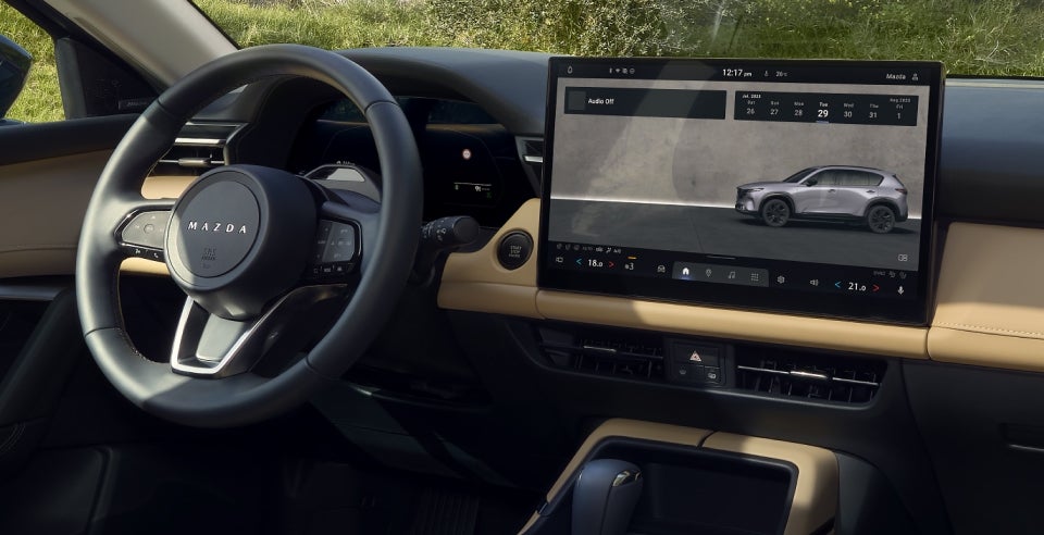 Interior of a Mazda CX-60 with a large infotainment screen displaying a gray SUV, and a dark steering wheel.