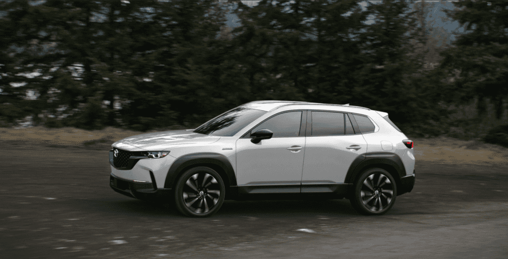 Light gray Mazda CX-50 traveling at speed, with a blur of dark trees and road behind it.
