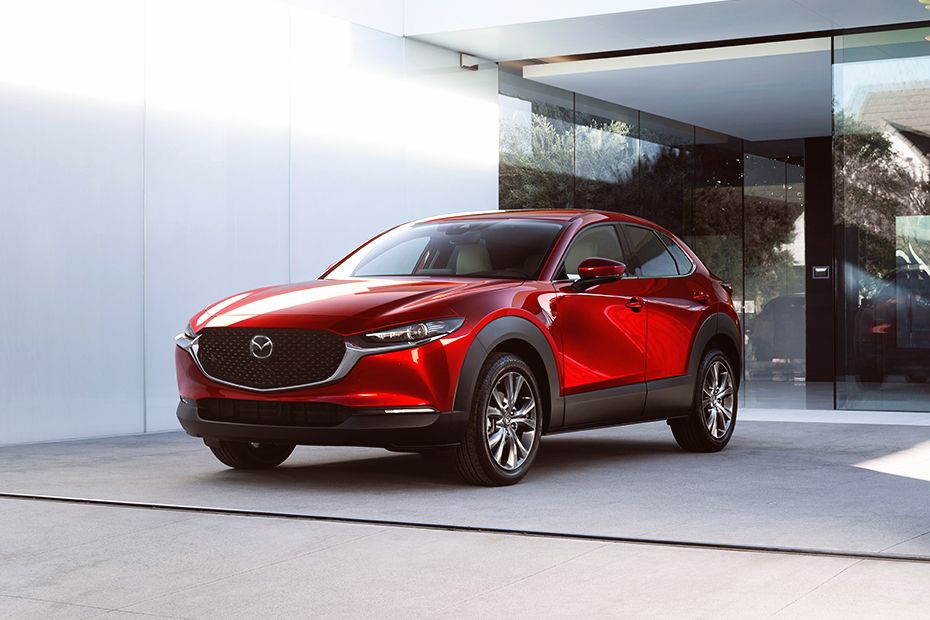 Front view of a shiny red Mazda CX-30 SUV parked outside a modern building with large glass windows.
